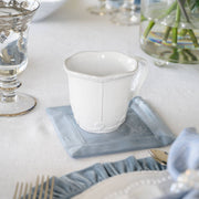 Arte Italica & Crown Linen Designs - Bella Bianca Beaded Mug on a blue cloth, showcasing its elegant beaded pattern and Italian stoneware craftsmanship.