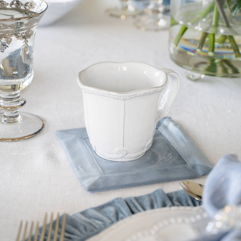 Arte Italica & Crown Linen Designs - Bella Bianca Beaded Mug on a blue cloth, showcasing its elegant beaded pattern and Italian stoneware craftsmanship.