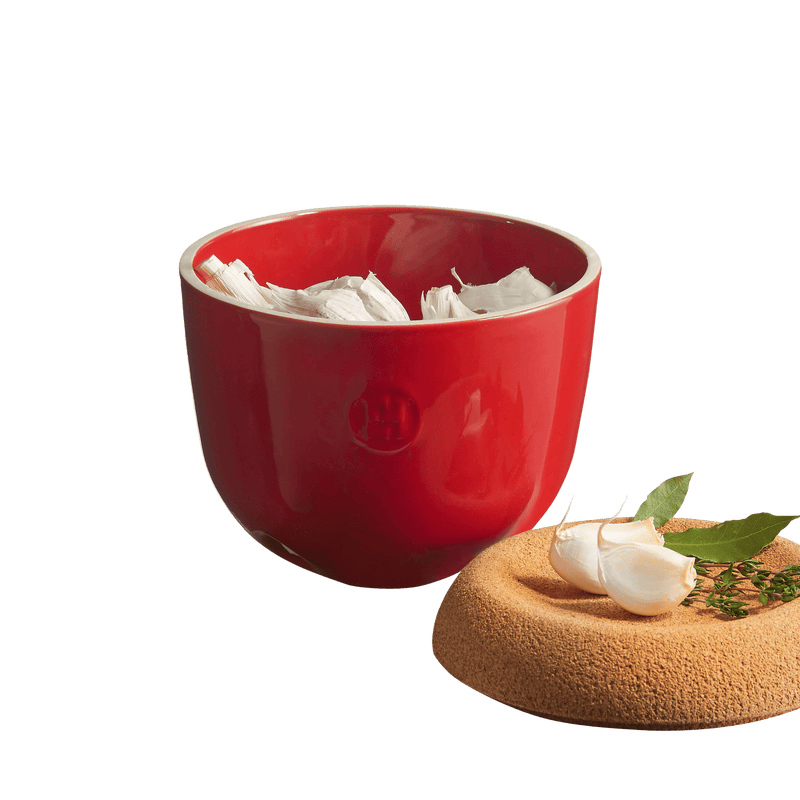 The Emile Henry Garlic Pot in Truffle, shown with garlic peels inside and its cork lid adorned with garlic cloves, bay leaves, and thyme, showcasing elegant kitchen storage.
