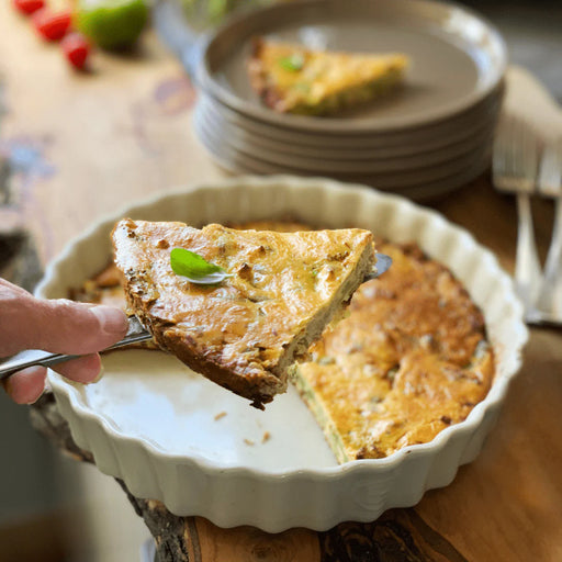 Emile Henry Deep Tart Dish, Clay, 1.2 QT, showcasing a freshly baked quiche with crisp edges, lifted from a fluted ceramic dish.