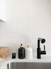 L'AVANT Collective - Fresh Linen Hand Soap in a matte black glass bottle on a bathroom counter, accompanied by a faucet and other bathroom accessories.