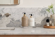 L'AVANT Collective Hand Lotion Ambre Santal on modern bathroom vanity, part of Athens Cooks' curated selection, offering luxury and plant-based nourishment in a stylish glass dispenser.