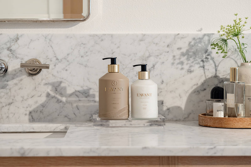 L'AVANT Collective Hand Lotion Ambre Santal on modern bathroom vanity, part of Athens Cooks' curated selection, offering luxury and plant-based nourishment in a stylish glass dispenser.