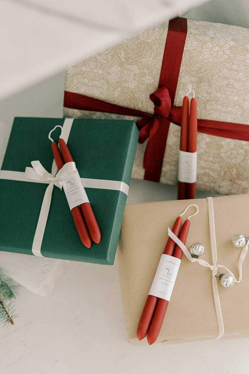 Mo&Co Home - Berry Red Dipped Beeswax Taper Candles atop wrapped gifts, showcasing elegant, handcrafted design with eco-conscious materials. Perfect for special occasions.
