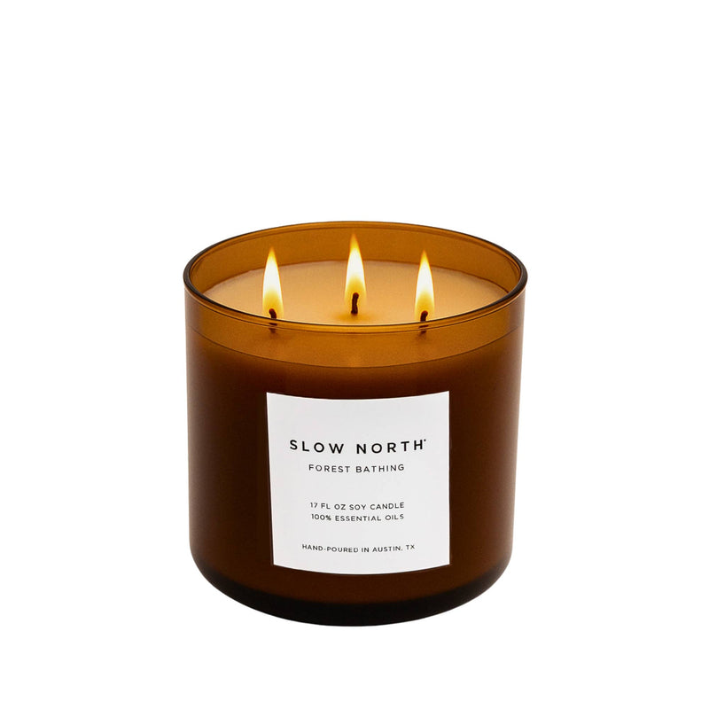 Slow North - Forest Bathing 3-Wick Soy Candle in amber jar, lit, with label detailing essential oils and hand-poured craftsmanship, perfect for creating a cozy, nature-inspired ambiance.