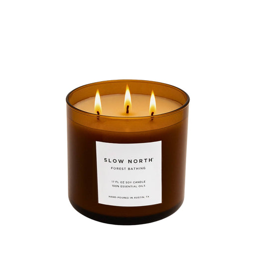 Slow North - Forest Bathing 3-Wick Soy Candle in amber jar, lit, with label detailing essential oils and hand-poured craftsmanship, perfect for creating a cozy, nature-inspired ambiance.