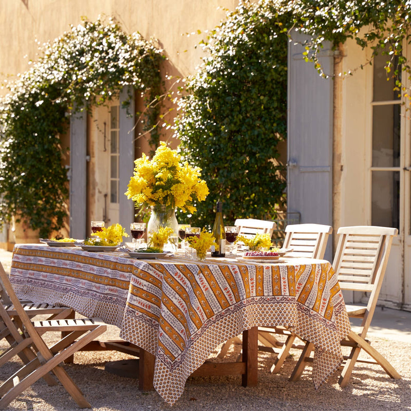 Couleur Nature - Provence Avignon Dijon & Blue Tablecloth: 59 x 86 on a sunlit outdoor dining setup with wine, yellow flowers, and place settings, evokes French elegance.
