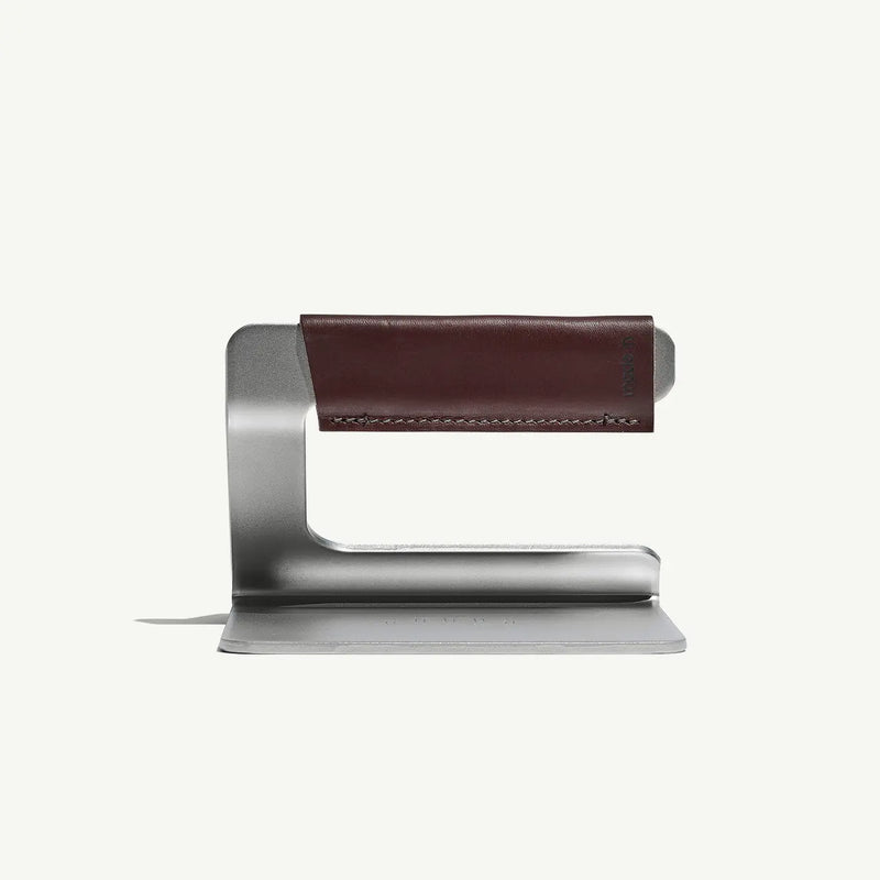 Minimalist headphone stand, Made In | Grill Press, features a bent metal design with a leather-wrapped top arm for hanging headphones.