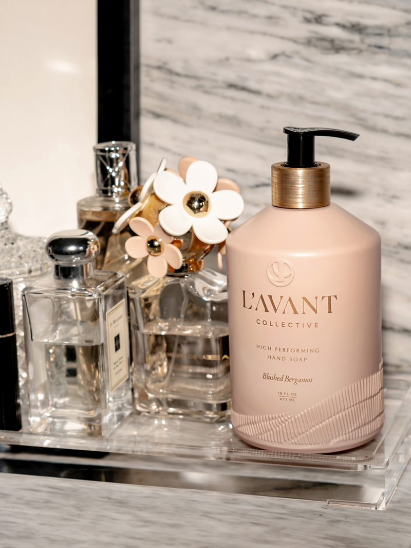 L'AVANT Collective - High Performing Hand Soap - Blushed Bergamot, elegantly presented in a blush pink glass bottle, alongside other toiletry bottles.