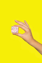 Malvi Mallow - Cotton Candy 4-Pack Marshmallows, Case of 12 Packs: A hand holds a pink marshmallow cube with sprinkles, showcasing its airy texture against a bright yellow background.