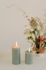 Mo&Co Home - 100% Beeswax Pillar Candles | Eucalyptus: 3x4 Inch, two candles beside a vase of flowers on a table.