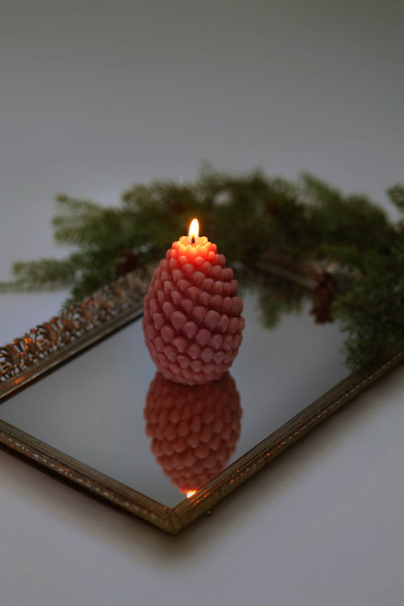 Mo&Co Home Exclusive: Sculpted Beeswax Pine Cone Candle on a gold-framed mirror, reflecting its elegant, festive shape, designed for holiday gatherings and gifting.