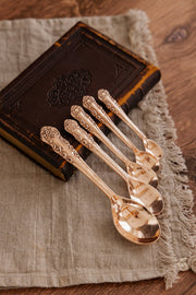 Coppermill Kitchen LLC - Coppermill Kitchen Vintage Inspired Measuring Spoon Set with ornate handles, on linen cloth, against an antique book, showcasing artisan copper craftsmanship.