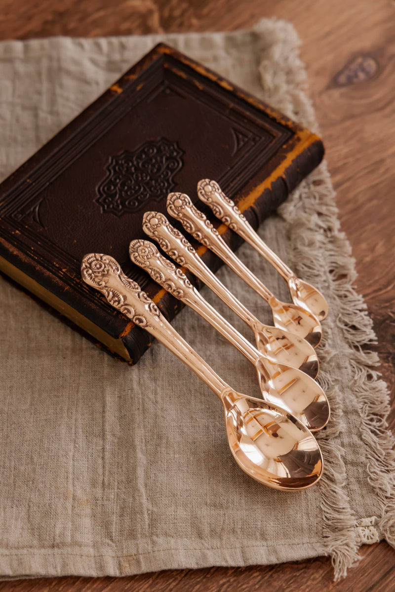 Coppermill Kitchen LLC - Coppermill Kitchen Vintage Inspired Measuring Spoon Set with ornate handles, on linen cloth, against an antique book, showcasing artisan copper craftsmanship.