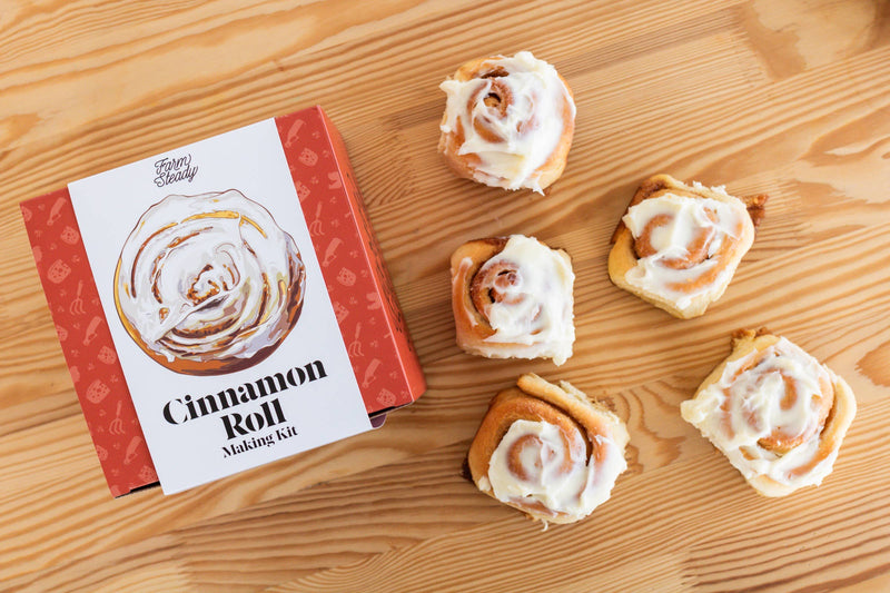 FarmSteady Cinnamon Roll Making Kit with five frosted cinnamon rolls, showcasing the baking mix, cinnamon sugar, and icing included for creating delicious homemade treats.