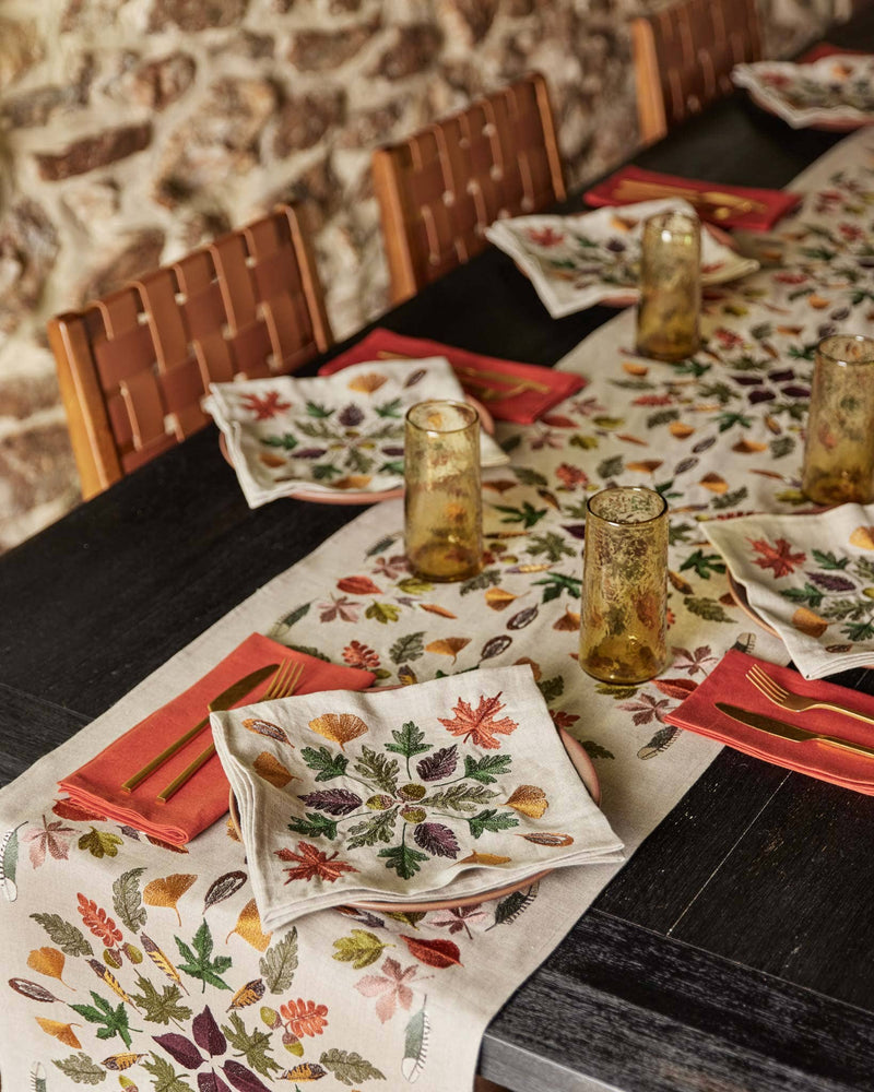 Coral & Tusk - Pressed Leaves Dinner Napkin, featuring intricate autumn leaf motifs, elegantly folded atop a pale pink plate in a rustic dining setup.