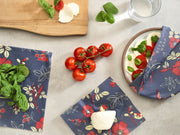 Bee's Wrap - Cut-to-Size Roll - Botanical Print is shown wrapping mozzarella and tomatoes in a Caprese setup on a kitchen counter with reusable food storage.
