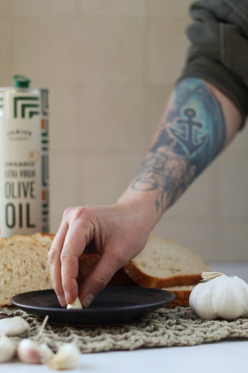 Gravesco Pottery - Garlic Grater Plate in Black with garlic, perfect for prepping dips and appetizers. Hand reaches to place clove, highlighting plate's textured surface.