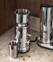 Aarke Coffee Grinder with sleek silver finish, displayed alongside a metal cup, showcasing its elegant design and functionality for coffee enthusiasts.