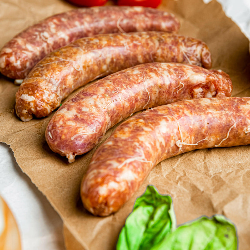 Rock House Creamery Sweet Italian Sausage Links on parchment with basil leaves; crafted from pasture-raised Berkshire pork, perfect for grilling or pasta.