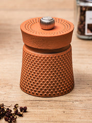 Peugeot | Bali Cast Iron Pepper Mill, Orange, on a wooden surface with peppercorns and a spice jar, highlighting its unique dimpled design inspired by traditional tea ceremonies.
