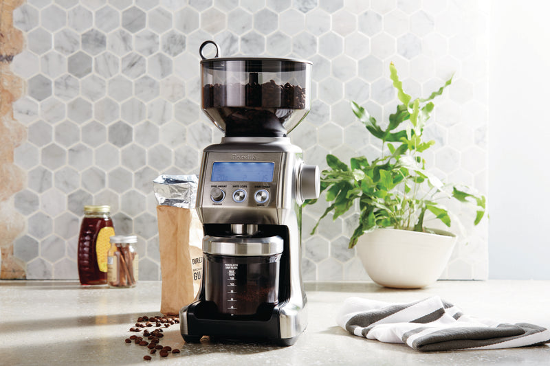 Breville Smart Grinder Pro on kitchen counter with beans, cinnamon, and honey nearby, showcasing its 60-settings feature for versatile coffee grinding.