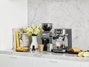 Breville | Smart Grinder Pro on a marble counter, surrounded by espresso essentials, enhancing a stylish breakfast setup with pastries and fresh daffodils.