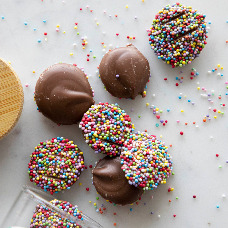 Hester & Cook | Buttons - Milk Chocolate shown as round cookies with multicolored sprinkles, ideal for snacking or gifting, displayed on a light surface.
