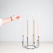 The Floral Society | Beacon Long-Stem Candelabra, Dune: Black metal candelabra with eight pastel tapers, one being lit by hand, showcasing handcrafted elegance from Athens Cooks.