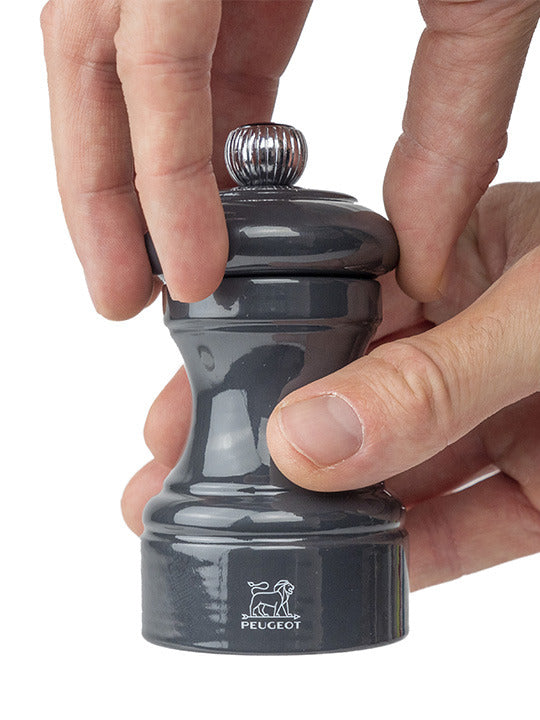 Hands adjusting Peugeot | Bistro Pepper Mill 4 Inches, Slate Grey, with a classic hourglass shape, featuring a silver knob for grinding size adjustment.