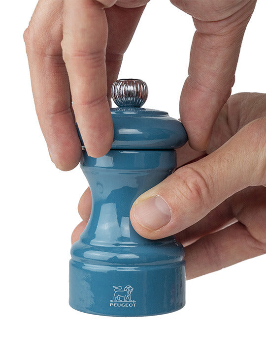 Hands twisting the top of the Peugeot | Bistro Pepper Mill in Pacific Blue, showcasing its elegant design and renowned grinding mechanism, perfect for culinary enthusiasts.
