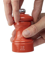 Hands grip and twist the top of the Peugeot | Bistro Pepper Mill, Terracotta, showcasing its ergonomic design and iconic Peugeot lion logo at the base.