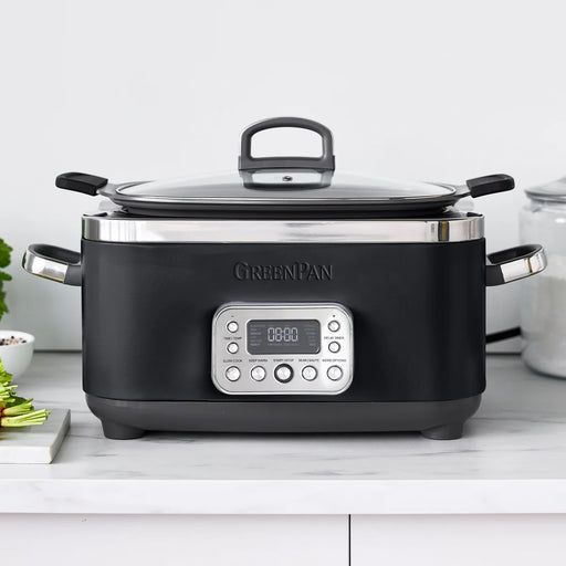 GreenPan Elite 14-in-1 6-Quart Slow Cooker with digital control panel and glass lid, displayed on a kitchen counter next to cooking ingredients.