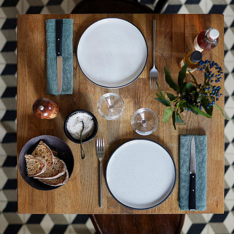 Opinel | Bon Appétit No.125 Steak & Table Knives Sets, Pro displayed on a wooden table, highlighting the black-handled knives atop green linen napkins in an elegant dining setup.