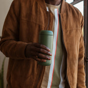 Person holding FELLOW | Carter Move Mug, Cargo Green / 16 oz, designed for maintaining beverage temperature with a True Taste ceramic interior, ideal for on-the-go coffee enjoyment.