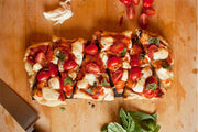 Wildwood Grilling | Cedar Grilling Planks displayed with a sliced pizza topped with tomatoes and basil, highlighting their use as unique serving platters.