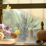 The Floral Society | Candle Holders, Grand, Matte White Tall sits on a sunlit windowsill, surrounded by floral arranging tools, reflecting Athens Cooks' curated kitchen elegance.