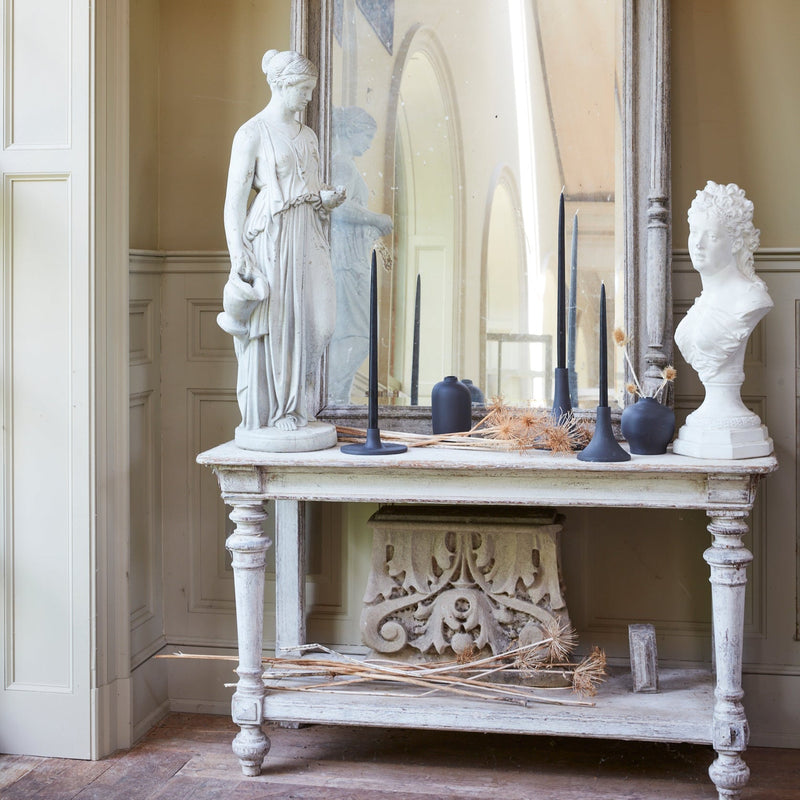 The Floral Society | Candle Holders, Grand, Matte White Tall displayed on a vintage console table, surrounded by classical sculptures and dried plants, embodying antique elegance.