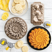 Nordic Ware | Citrus Blossom Loaf Pan displayed among baking pans and cookies, showcasing its 6-cup capacity for creating sculptural quick breads and loaf cakes.