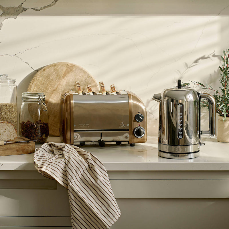 Dualit | 4 Slice Classic Toaster, Copper, popping bread, on a breakfast-ready kitchen counter with a kettle, bread, and pantry jars.
