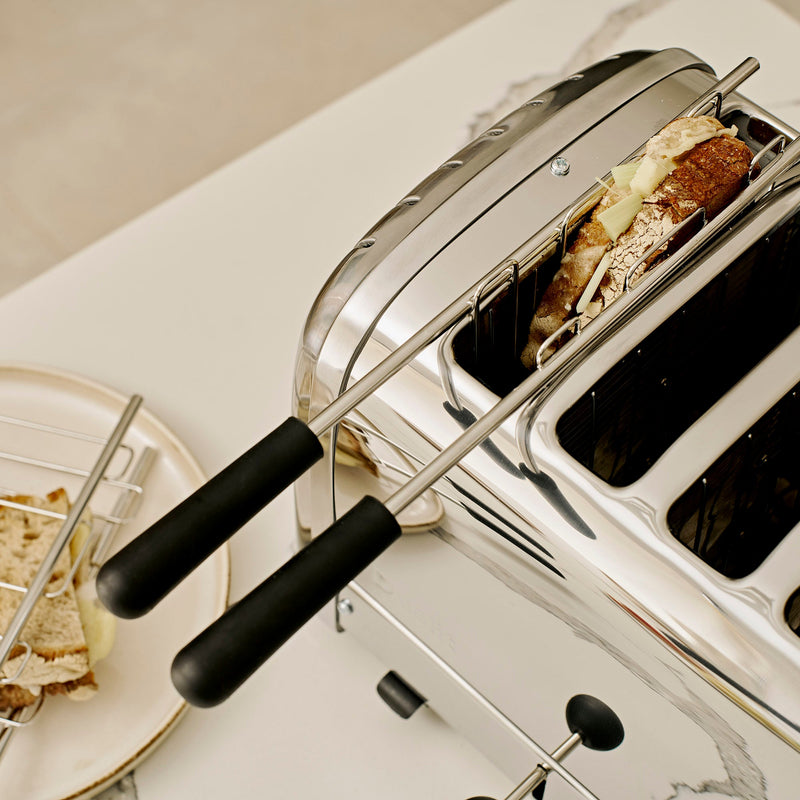Dualit | 4 Slice Classic Toaster, Polished, with metal tongs holding a cheese-filled baguette slice, showcasing its durable design and energy-efficient, adjustable features.