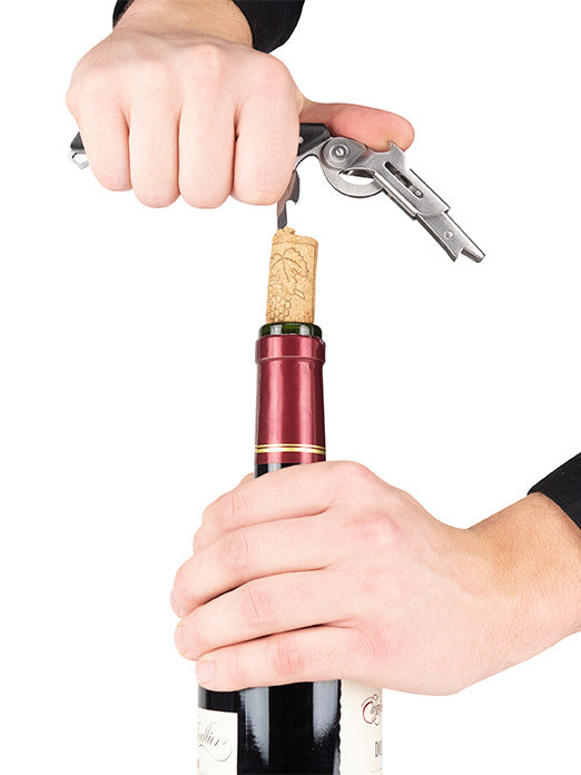 Hands using the Peugeot Clavelin Sommelier Corkscrew to open a wine bottle, showcasing its patented handle mechanism for effortless cork removal.