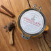 Los Poblanos | TESTER Chocolate de Nuevo Mexico jar on a wooden surface, surrounded by cinnamon sticks and a spoon with brown powder, emphasizing its artisanal quality.