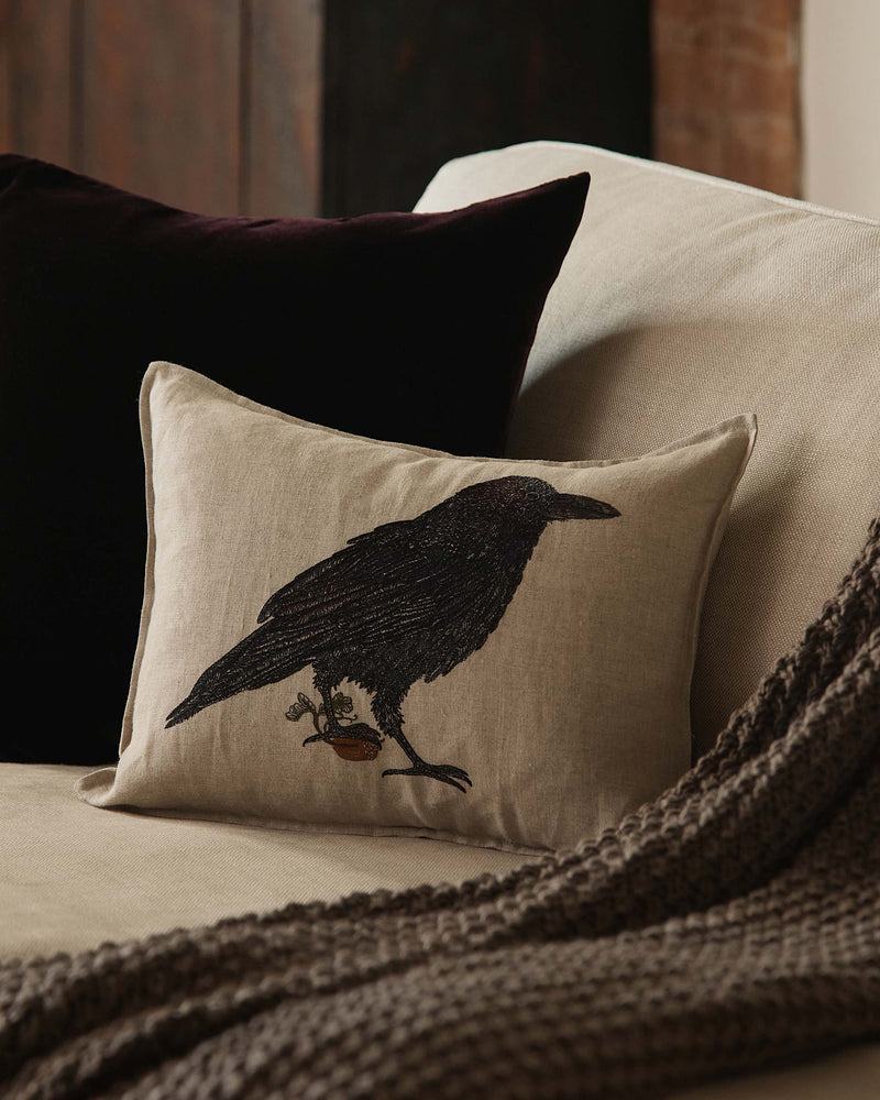 Coral & Tusk | Blackbird with Acorn Pillow: A light-beige throw pillow featuring an embroidered blackbird on an acorn, paired with a velvet pillow and knit throw.