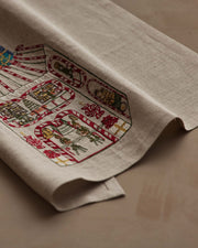 Coral & Tusk | Toy Workshop Tea Towel: Natural-linen with embroidered candy-cane borders showcasing festive scenes like Santa’s helpers and gifts, ideal for holiday kitchen decor.