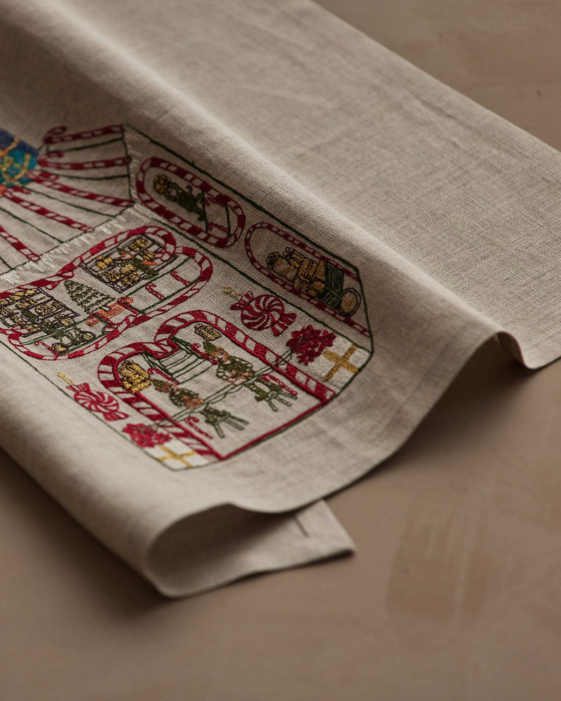 Coral & Tusk | Toy Workshop Tea Towel: Natural-linen with embroidered candy-cane borders showcasing festive scenes like Santa’s helpers and gifts, ideal for holiday kitchen decor.