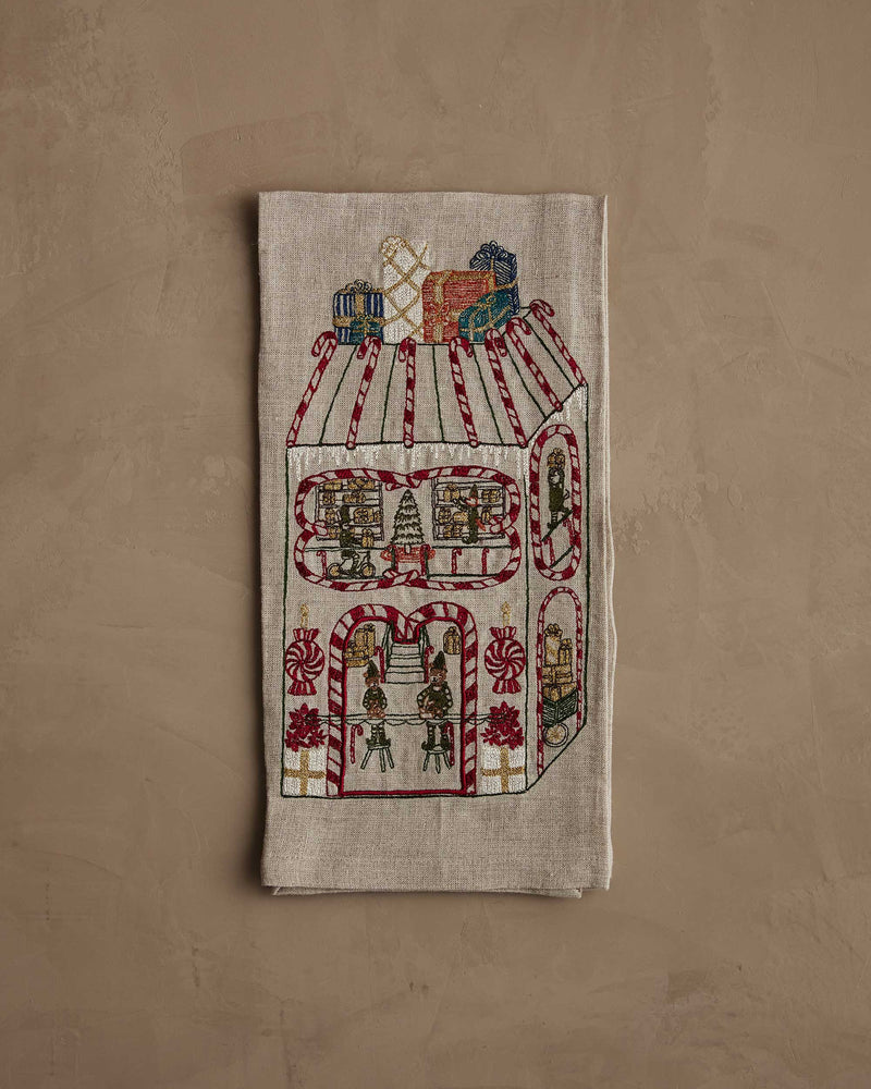 Coral & Tusk | Toy Workshop Tea Towel featuring embroidered whimsical gingerbread house scene with elves, candy accents, and gifts, perfect for a festive kitchen decor.