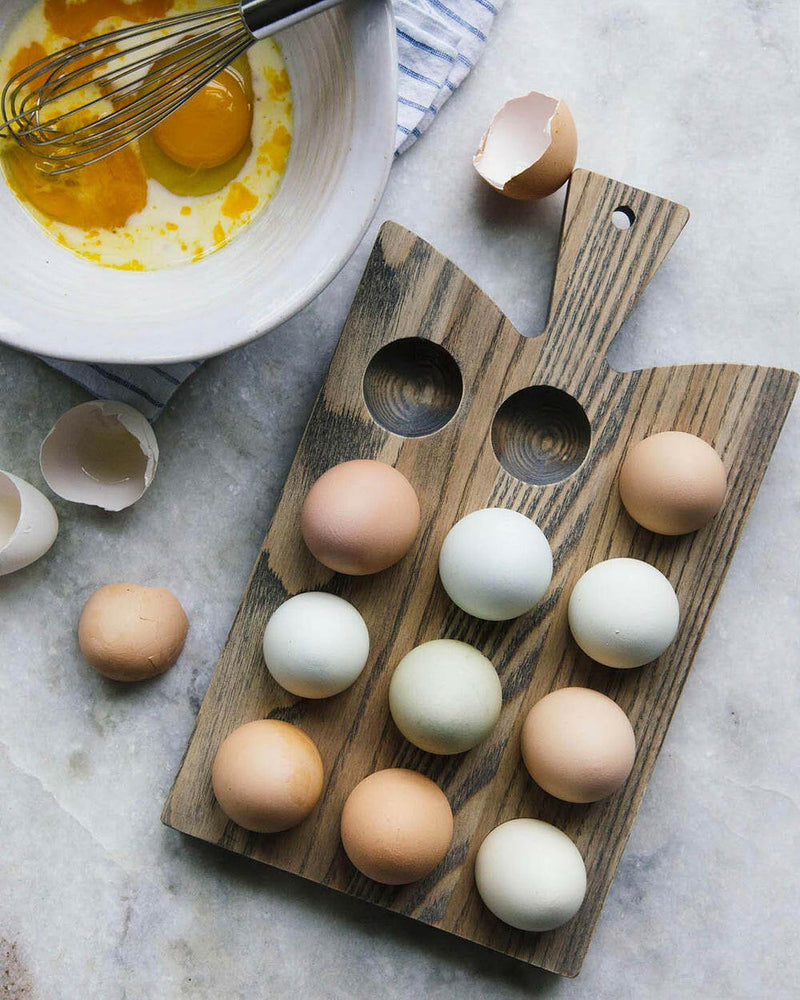 Farmhouse Pottery Crafted Wooden Egg Board displaying a dozen varied eggs, with a mixing bowl and whisk nearby, showcasing its kitchen utility.