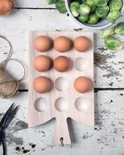 Farmhouse Pottery | Crafted Wooden Egg Board Cornish - White, displayed with eggs, Brussels sprouts, onion, jute twine, and scissors on a rustic kitchen tabletop.