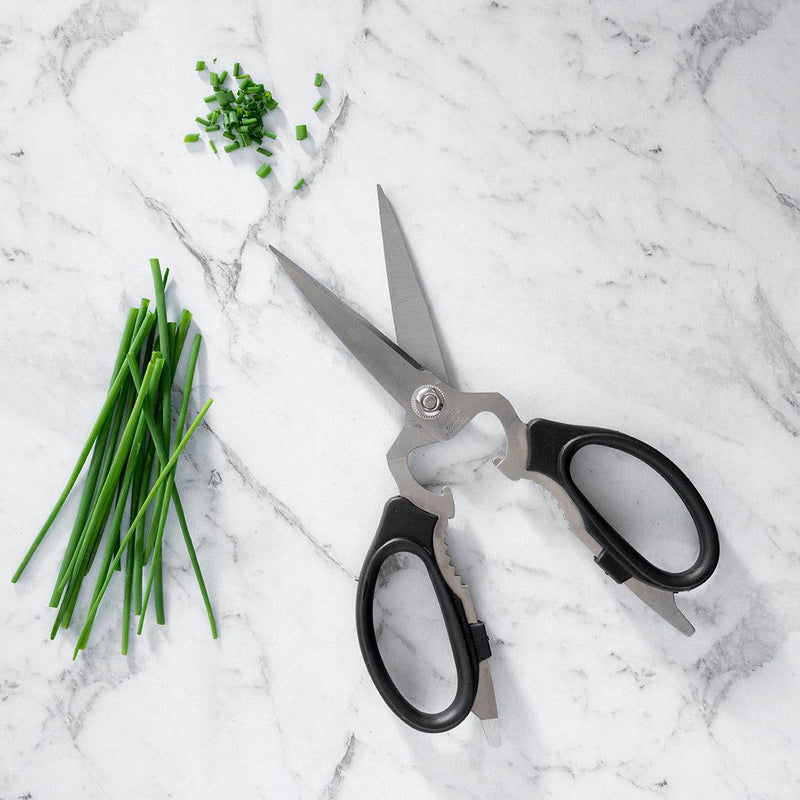 Messermeister | Black Take-Apart Kitchen Scissors, 8, lie open on marble next to snipped chives, showcasing ergonomic design and micro-serrated blades for precise cutting.